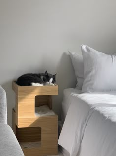 a black and white cat laying on top of a wooden shelf next to a bed