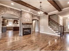 an empty living room with wood flooring and brick fireplace in the middle of it