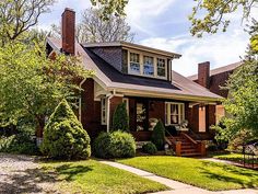 a brown house with trees and bushes in the front yard