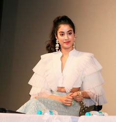 a woman in a white top and blue skirt sitting on a chair with her hands folded