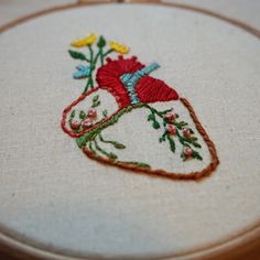 embroidered heart with flowers and leaves on white fabric in wooden frame, closeup view