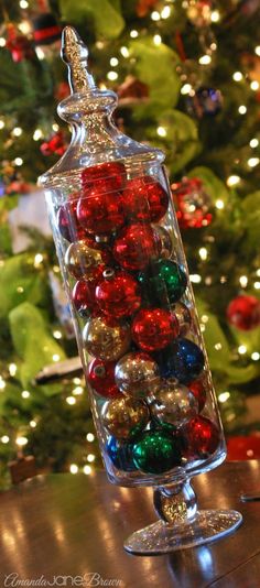 a glass container filled with christmas ornaments on top of a table next to a christmas tree