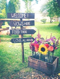 a wooden crate filled with flowers sitting on top of a grass covered field next to a sign