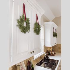 two wreaths hanging on the wall above a stove top in a kitchen with white cabinets