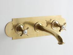 a brass faucet with two handles on a white wall