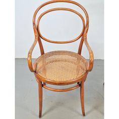 a wooden chair with wicker seat and armrests, on a gray floor