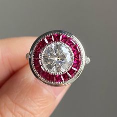 a close up of a person's hand holding a diamond and ruby ring