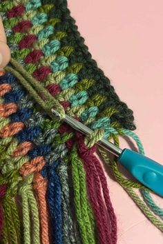 someone is crocheting the ends of a multicolored scarf with scissors and yarn