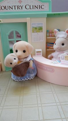 two stuffed animals are sitting in front of a doll house with a sink and toilet