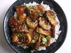 a black plate topped with rice and meat covered in sauce