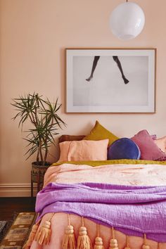 a bed with pink sheets and pillows in a bedroom next to a potted plant