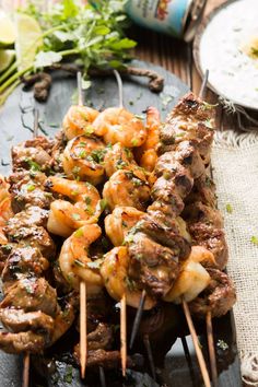 several skewers of meat and shrimp are on a table with other food items