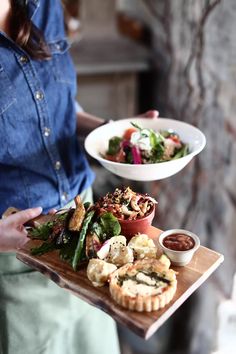 a woman holding a tray with food on it and another plate full of food in the background