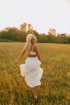 a woman in a white dress is walking through the grass