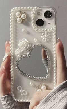 a woman holding up a cell phone case with pearls and hearts on the back,