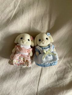 two small stuffed animals sitting next to each other on a white sheet covered bed together