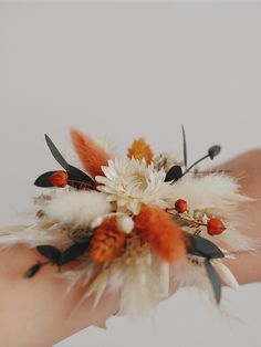 a woman's hand holding a flower and feather corsage