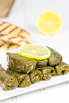 stuffed grape leaves on a plate with lemon wedges and pita bread in the background