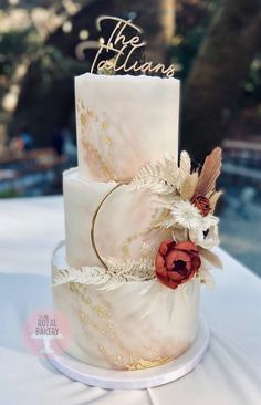 a three tiered wedding cake decorated with flowers and gold leaf accents is sitting on a white tablecloth