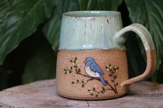 a ceramic mug with a blue bird painted on the side and green leaves behind it