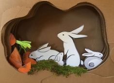 a cardboard box filled with paper cutouts of rabbits and carrots on top of moss