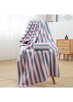 a pink and blue striped blanket sitting on top of a wooden chair next to a window