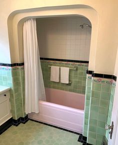 a bathroom with green and white tiles on the floor, tub, sink and mirror