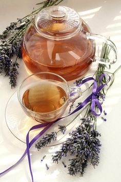 a glass tea pot filled with liquid next to lavender sprigs on a plate