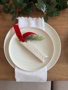 a white plate topped with a red ribbon and a place setting on top of a wooden table