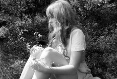 black and white photograph of a woman sitting on the ground with her legs crossed, looking at something