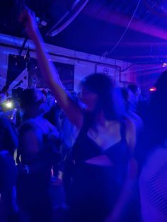 a group of people dancing in a dark room with blue lights on the ceiling and one woman holding her arm up