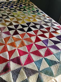 a crocheted blanket with multicolored triangles on it sitting on top of a bed