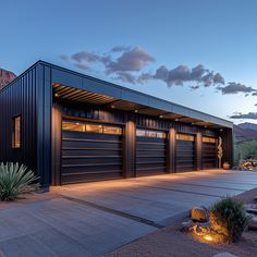 a large garage with two cars parked in front of it at night, surrounded by rocks and cactus