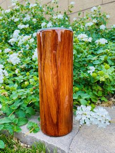 a wooden vase sitting on top of a cement slab in front of some bushes and flowers