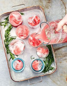 a tray filled with drinks and ice cubes on top of a cement floor next to a person's hand