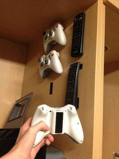 a person is holding a video game controller in front of some remote controls on the wall