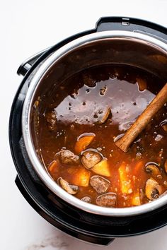 a wooden spoon in a pot filled with stew and potatoes on a white table top