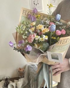 a woman holding a bouquet of flowers in front of a white wall with pictures on it