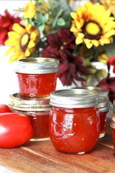 four jars of tomato jam on a cutting board with flowers in the background