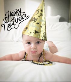 a baby wearing a party hat laying on top of a bed with the caption happy new year