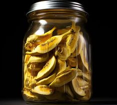 a jar filled with sliced bananas sitting on top of a table next to a black background