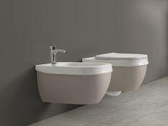 two white toilets sitting next to each other in a room with gray walls and tile flooring