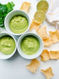 three bowls filled with guacamole surrounded by tortilla chips and cilantro