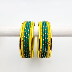 Illuminate your style with the Roshani Banglez Box, a brilliant collection designed for the festive season! This vibrant set includes a stunning array of bangles in matte yellow, teal, lime green, metallic yellow, mehndi green, and gold. Framed by four majestic gold-plated zircon stone bangles, perfect for adding a touch of elegance to any occasion. With a variety of matte, glitter, and metallic finishes, the Roshani Box lets you mix and match to create endless unique sets. These bangles are versatile enough to wear often, making them ideal for brightening your own collection or gifting to someone special! *free matching bindi included *please note bangle boxes are final sale. *colour tones may appear slightly different in person than on screen. Luxury Multicolor Bangle For Festive Occasions, Festive Green Bangle Jewelry, Green Bangle For Festivals, Festive Adjustable Yellow Bangle, Green Bollywood Bangle For Festivals, Red Green Bangles Set, Bangle Box, Stone Bangle, Bangles Jewelry