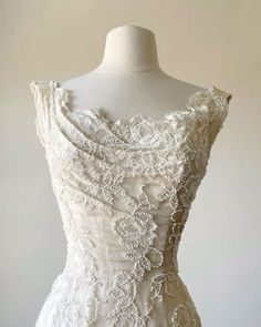 a white wedding dress on a mannequin with beading and flowers in the back