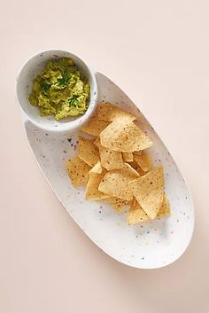 a plate with chips and guacamole on it next to a small bowl