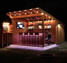 a woman sitting at a bar in the middle of a yard with lights on it