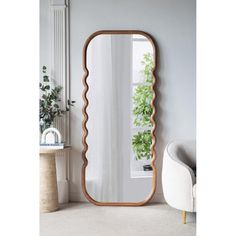 a large mirror sitting on top of a white floor next to a chair and potted plant