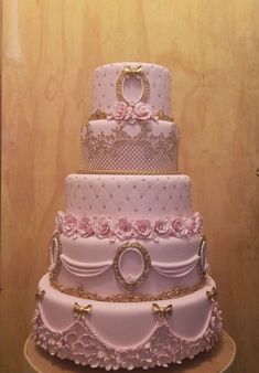 a three tiered wedding cake with pink flowers and gold trimmings on a wooden table