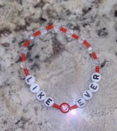 a red and white beaded bracelet with the word luck never on it, sitting on a marble surface